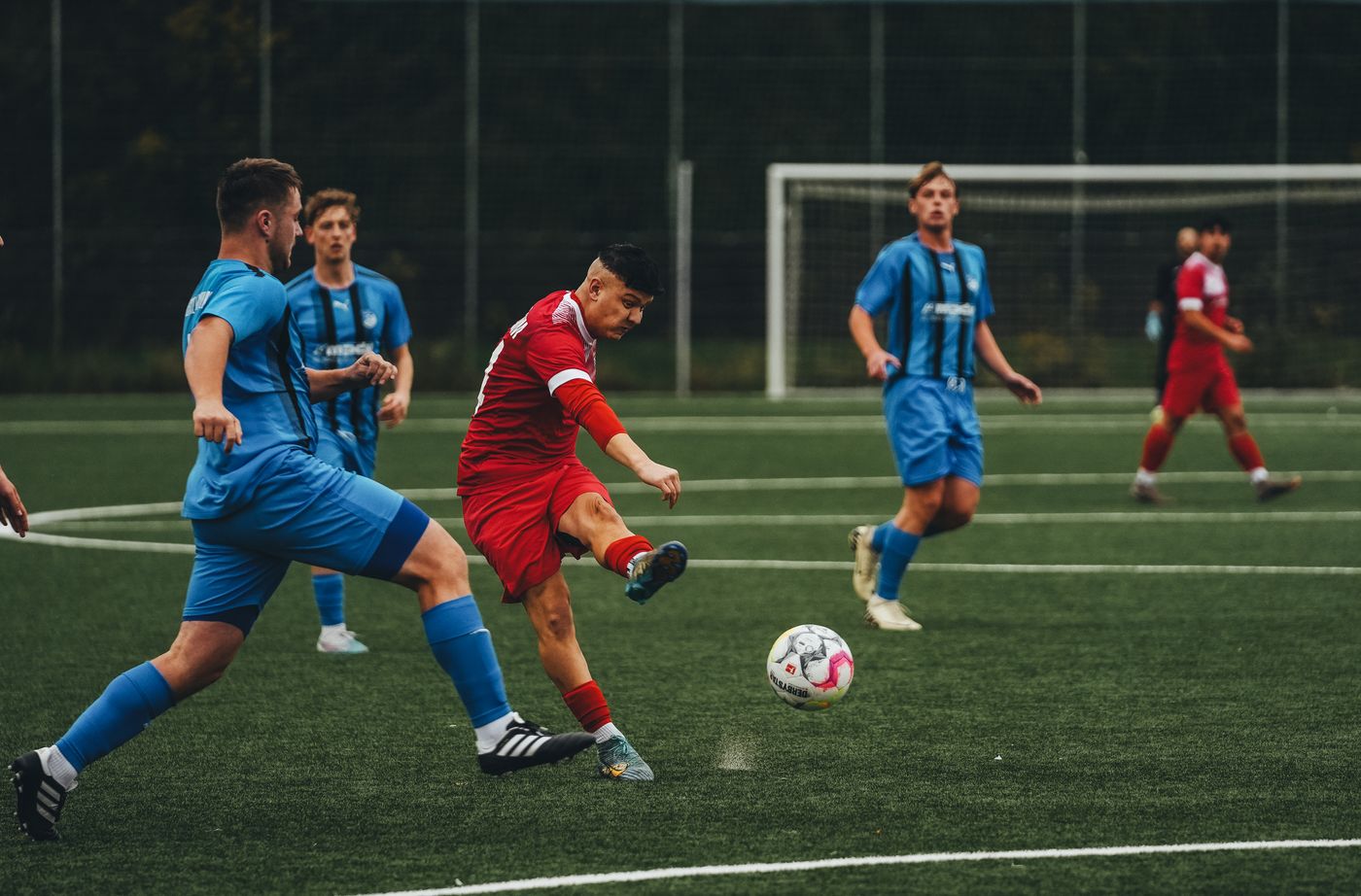 Teams in blue and red kit facing off on a grass pitch