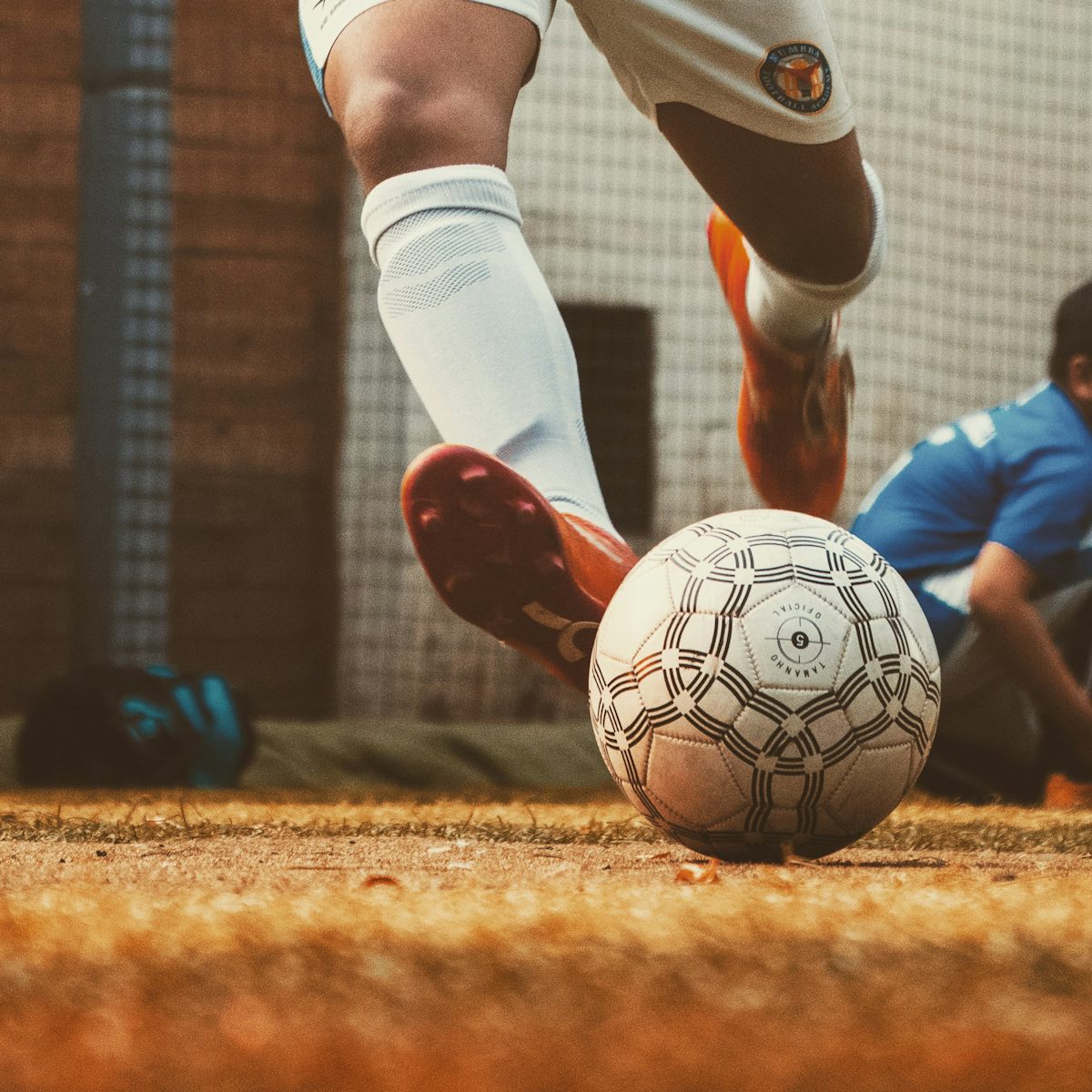 Ground-level view of a player striking a ball on a worn pitch