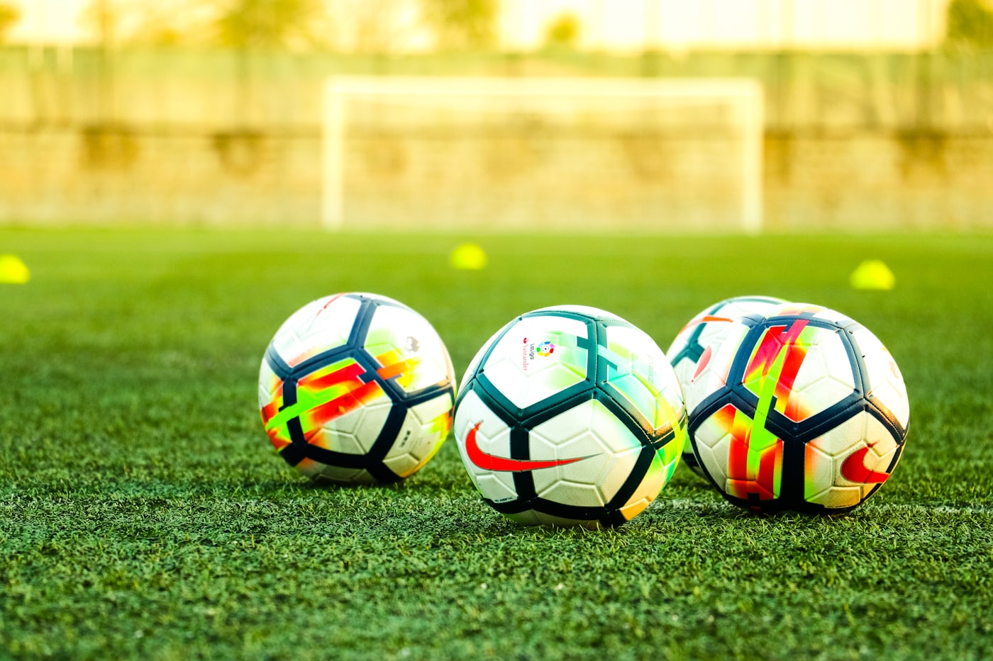 Three match balls lined up on a training pitch in front of a goal
